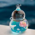 Gros plan du pendentif gourde transparent rempli d'huile avec lotus rose et paillettes. - Calebasse