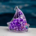 Gros plan sur le pendentif voilier en acrylique transparent rempli de perles violettes. - Violet