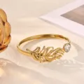 Gold open cuff bracelet featuring a detailed feather design and a sparkling crystal accent. - Exquisite Feather Style (B2357G-1)