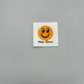 Close up of a DIY clothing woven cloth label featuring a cute smiling face and text detail. - sy001