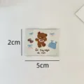 Gros plan d'étiquette tissée avec broderie d'ours mignon et dimensions pour travaux manuels. - Ours Graffiti Nœud Papillon