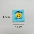 Close-up detail shot of a blue woven patch featuring a yellow smiley face and denim text. - zm007