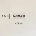 Custom sewing label detail closeup, white woven cloth tag with cute black text and heart logo. - Koki Style (zm306)
