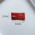 Etichetta tessuta rossa con viso sorridente e testo DIY accessori per abbigliamento 2.5x4.8cm - Stile SMILE Base Rossa Sorriso Giallo (zm122)