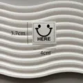 White woven patch label with a black smiley face and HERE print for clothing decoration. - Here Smiley Face White