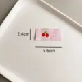 Vue détaillée de l'étiquette en tissu rose brodée de cerises avec des dimensions claires. - zm029