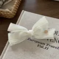 Elegant white fabric bow hair clip detail shot, featuring lace trim and gold charm. - Spring Clips