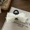 Closeup detail of a white lace bow hair claw clip with a gold heart charm on a vintage book. - Hair Claw