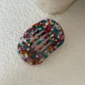 Detailopname van ovaal haarspeldje met kleurrijk terrazzo patroon, stijlvol accessoire. - Meerkleurig