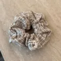 Nahaufnahme eines süßen braunen Karo-Stoff-Haargummis, weiches flauschiges Mode-Accessoire. - Khaki Kariert Haargummi