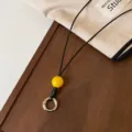 Vista detallada de correa para gafas de cuero negro con cuenta amarilla y anillo metálico. - Cuentas Amarillas