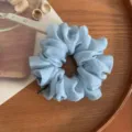 Vista detallada de un coletero de gasa azul claro en bandeja de madera con accesorios elegantes. - Azul