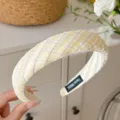 Gros plan d'un serre-tête en tissu écossais jaune, montrant une texture fine et une étiquette. - Jaune