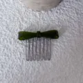 Close-up of the dark green acetate bow hair comb, showing fine texture and metal teeth. - Green