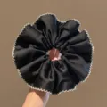 Gedetailleerde close-up van een chique zwarte satijnen haarscrunchie met witte geschulpte rand. - Klassiek Haarelastiekje / Zwarte scrunchie
