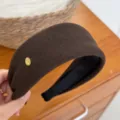 Dettaglio di un cerchietto in velluto marrone con etichetta dorata, elegante accessorio per capelli. - bordo largo / Marrone scuro