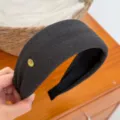Primo piano dettagliato di un cerchietto per capelli largo in tessuto grigio scuro con logo dorato. - bordo largo / Grigio