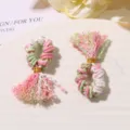Primo piano dettagliato di mini nappe intrecciate a mano con fili colorati e filo d'oro. - verde rosa