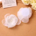 Close up of white mesh fabric flower hair clip detail showing pearl center and felt backing. - Beige