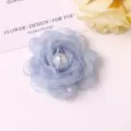 Close-up of light blue mesh fabric camellia flower with faux pearls for DIY crafts and accessories. - Blue