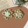 Nahaufnahme handgemachter perlenbesetzter Blumen-DIY-Accessoires in frischem Gruen und Weiss. - Blume