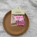 Dettaglio di graziose mollette per capelli rosa in sacchetto trasparente su piatto legno. - 5 Pezzi/Confezione / Rosa