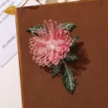 Primo piano dettagliato di una spilla con fiore rosa ricamato e perle di cristallo. - Rosa
