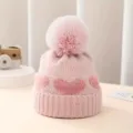 Baby knit hat detail showing pink jacquard heart pattern and soft plush pompom texture. - Pink