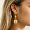 Close-up shot of gold geometric statement earrings featuring a shell top and chunky drops. - Gold