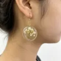 Close-up detail of a round resin dried flower pendant earring with a golden metal rim. - 5#