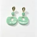 Close-up detail showing the gold cowrie shell stud and green resin pendant of the earrings. - Style 1