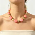 Close-up detail of the pink resin statement necklace with golden metal beads for women. - Pink