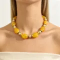 Close-up detail of the chunky yellow resin and gold metal bead statement necklace worn on neck. - Yellow