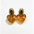 Detailed close-up of colorful heart resin earrings with textured gold metal top studs. - Amber