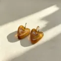 Close-up detail of detachable brown resin heart pendant with stainless steel hoop earrings. - Amber