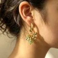 Close-up detail of gold metal flower earrings with green bead pendant, elegant and stylish. - Green