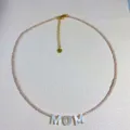 Detail view of dainty beaded choker necklace with shell MOM letter pendant and gold chain. - MOM