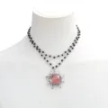 Detailed view of the double-layer black beaded necklace featuring a silver sun pendant. - Pink