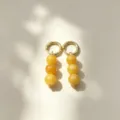 Close-up detail of golden hoop earrings featuring yellow stone beads hanging in soft natural light. - No.6 Gold