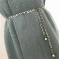 Detail shot of a stylish silver metal chain belt with elegant oval links and hanging ball pendants. - Style A Waist Chain / White K