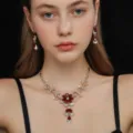 Primo piano dettagliato di collana floreale dorata e orecchini abbinati con pietre rosse. - Stile Foglia di Fiore (80803603)