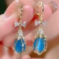 Close-up detail of exquisite golden bow and blue teardrop pendant earrings, sparkling design. - 7426 Blue
