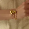 Primo piano dettagliato di un elegante bracciale rigido dorato con due sfere lisce. - Bracciale Rigido (0052-4) / Oro