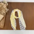 Detailed view of yellow polka dot scarf with white lace trim and pearl ring accessory. - Yellow