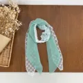 Detailed view of green polka dot scarf with delicate white lace trim and pearl buckle accessory. - Green