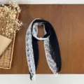 Detailed view of the elegant black and white lace spliced scarf with pearl buckle accessory. - Black