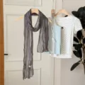 Detailed view of the elegant grey crinkled long scarf hanging with a stylish summer outfit. - Gray