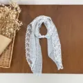 Close-up detail of blue plaid lace scarf with elegant white lace trim and pearl buckle. - Blue
