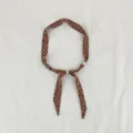 Detailopname van de retro bruine bloemenprint sjaal ketting met delicate kraalaccenten. - Ster Bloemen Bruin