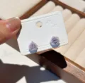 Primer plano detallado de pendientes de botón de rosa violeta claro en tarjeta blanca. - Rosa Púrpura